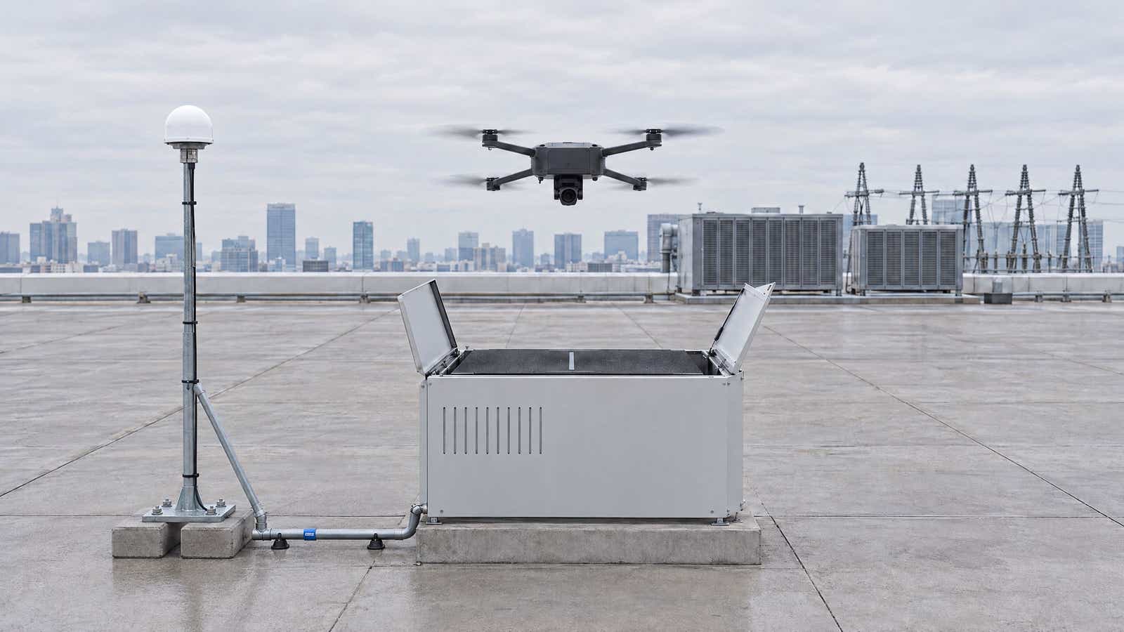 Illustration of an automated drone dock on an industrial rooftop, with a drone above it and a pole-mounted GNSS antenna cabled to it.