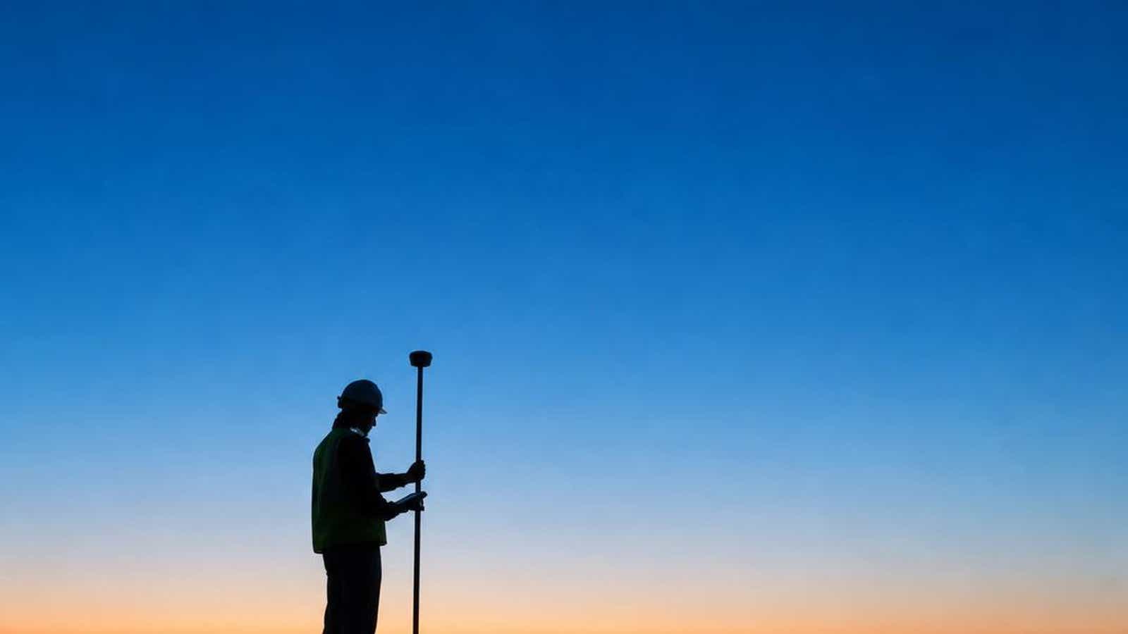 Silhouette of a surveyor holding a GNSS rover pole at twilight, the field work behind every land survey